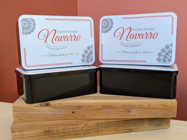 Petites boîtes noires rectangulaires avec couvercle blanc illustré du logo Navarro et dentelles provençales.